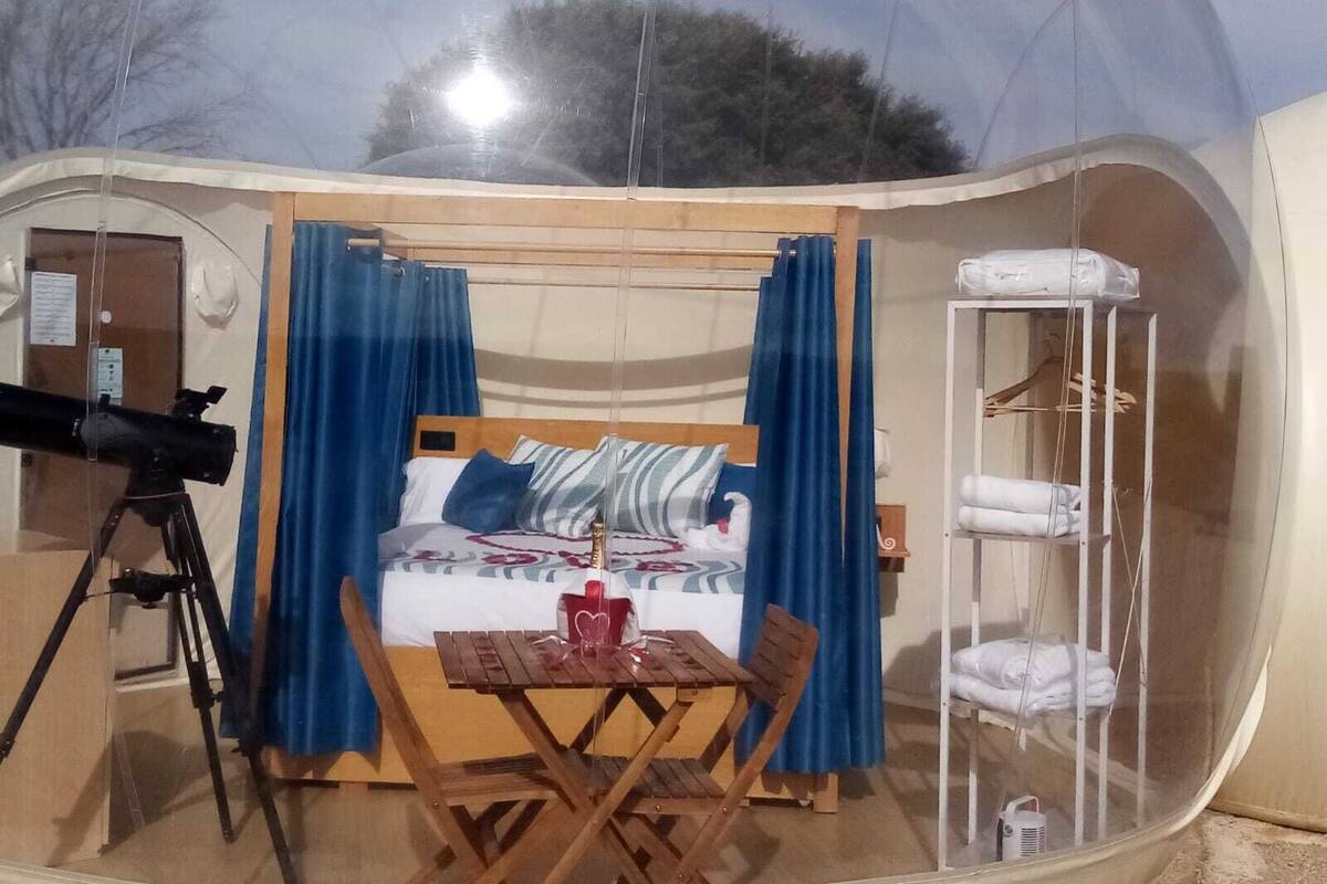 Un cuarto con tienda de campaña, una cama, una mesa y un telescopio.