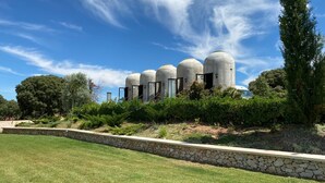 Una hilera de estructuras cilíndricas con puertas, rodeadas de un jardín ajardinado con un muro de contención de piedra y una zona de césped.