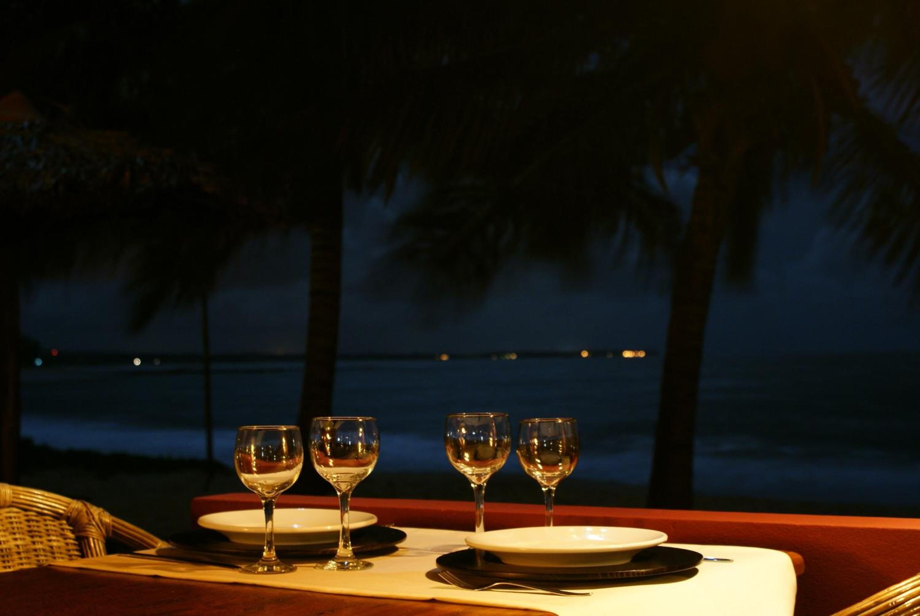 A table set for three with wine glasses and plates, overlooking a beach at night.