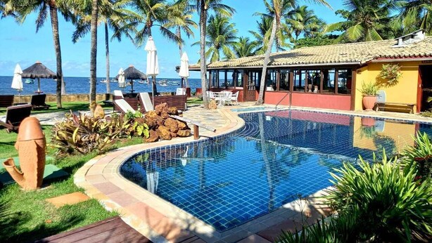 Piscina con borde de azulejos, rodeada de palmeras y sillas de descanso.