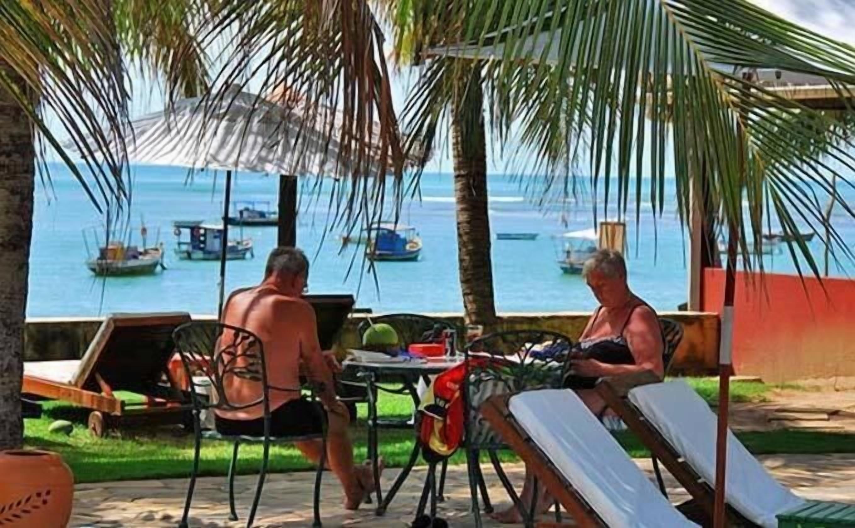 Duas pessoas sentadas numa mesa ao ar livre, com vista para o mar e barcos.