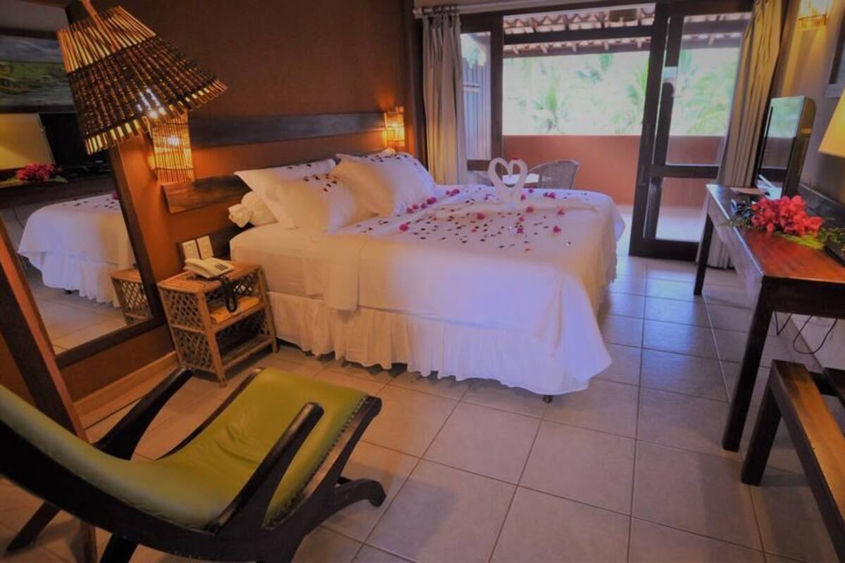 A hotel room with a bed, a chair, a desk, a lamp, and a view of the outdoors.