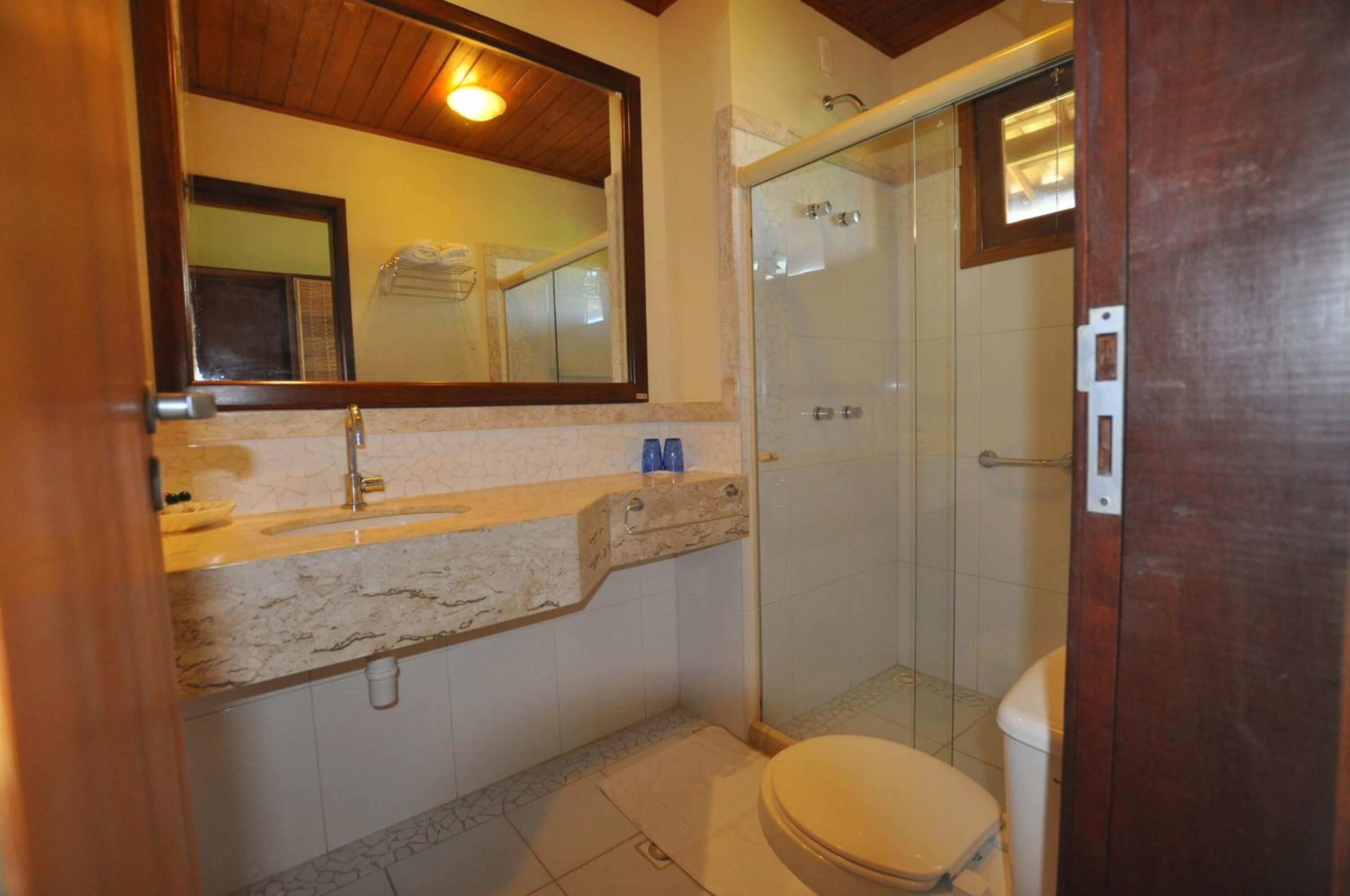 Et badeværelse med vask i marmor, et spejl, en bruseniche og et toilet.