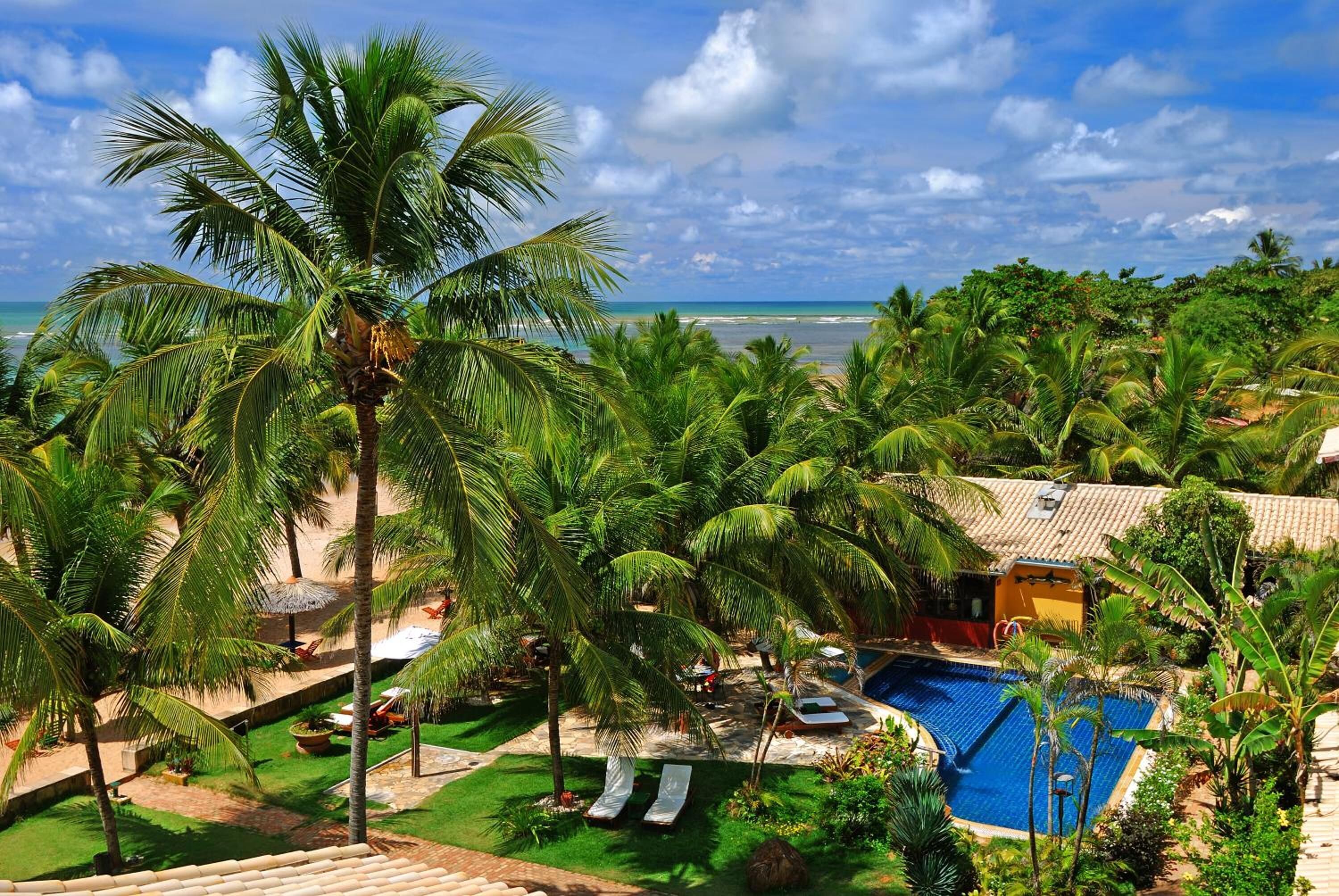 Um resort com piscina, palmeiras e vista para o oceano.