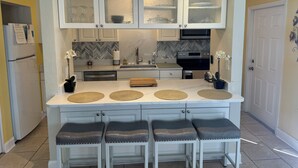 A modern kitchen with white cabinets, a central island with stools, a built-in oven, and a microwave.