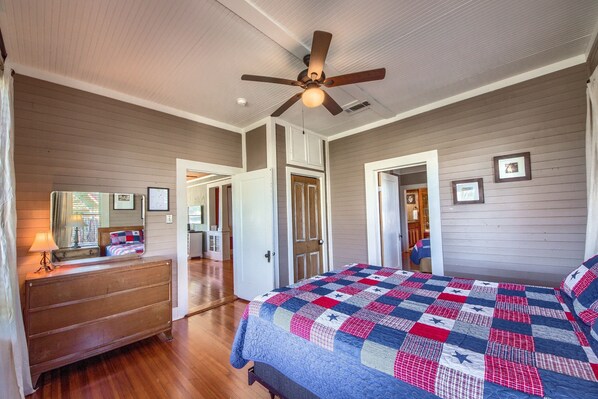 A bedroom with a wooden dresser, a bed with a quilt, a ceiling fan, and a door leading to another room. - Star Haus DT 292 5 Bedroom Home by RedAwning (New Braunfels)