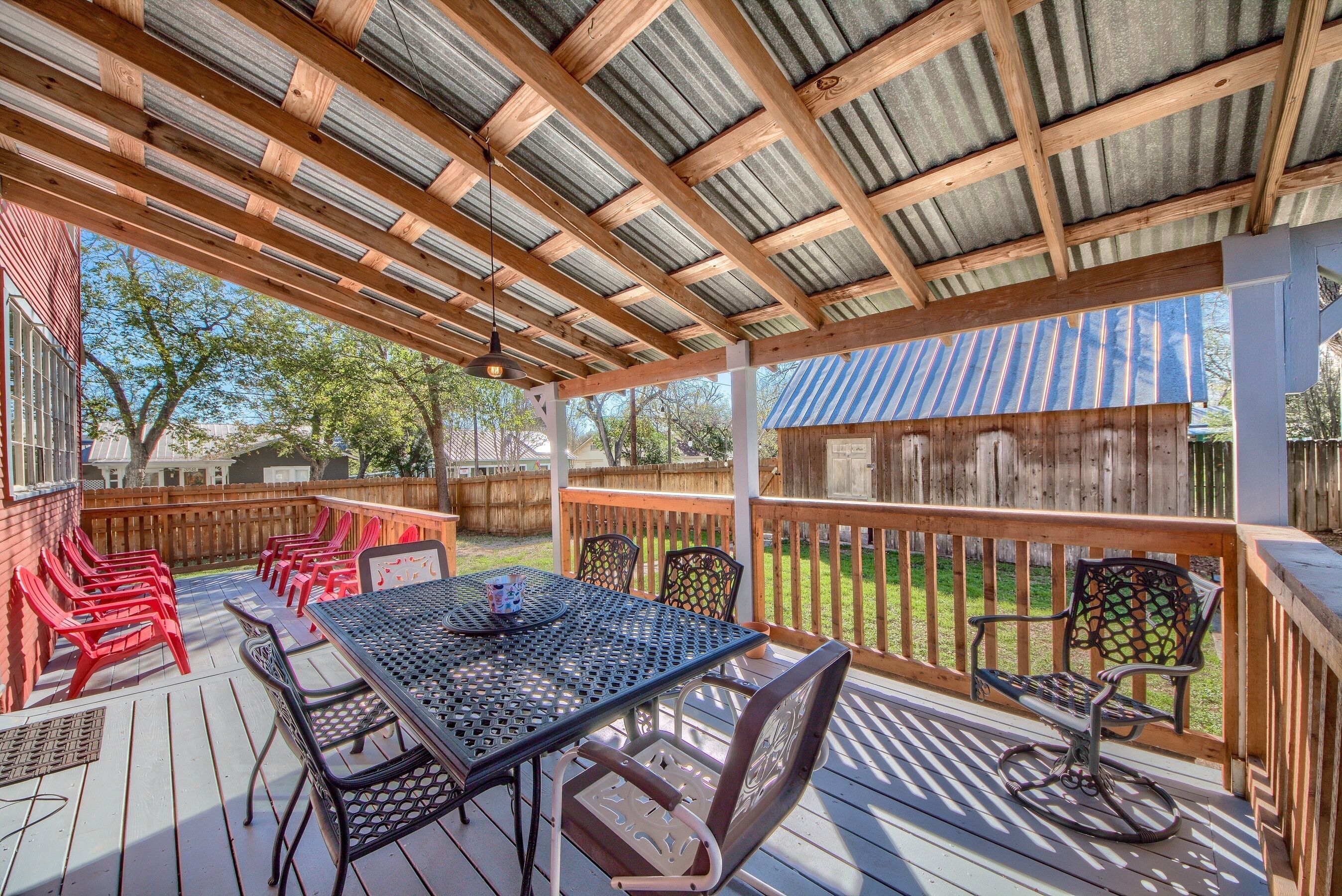 A covered outdoor deck with a table and chairs, a wooden fence, and a view of the backyard.