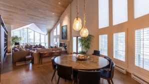 A spacious living room with a round dining table, a high ceiling with exposed beams, and large windows with blinds. - Northwoods Private Penthouse with Effortless Ski-In Ski-Out Access by RedAwning (Vail)