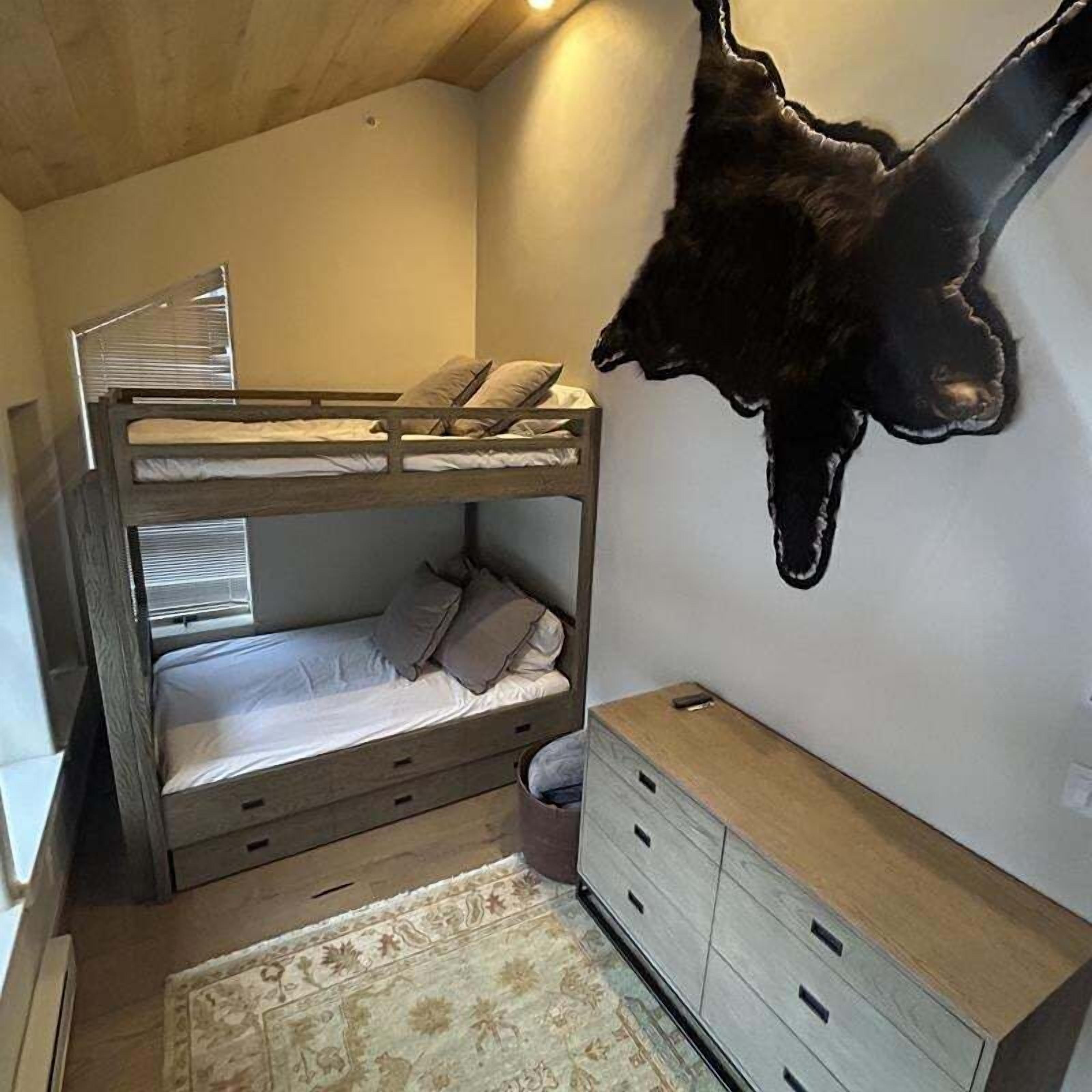 Habitación con literas, cabecera de madera, cómoda pequeña y alfombra en el suelo.