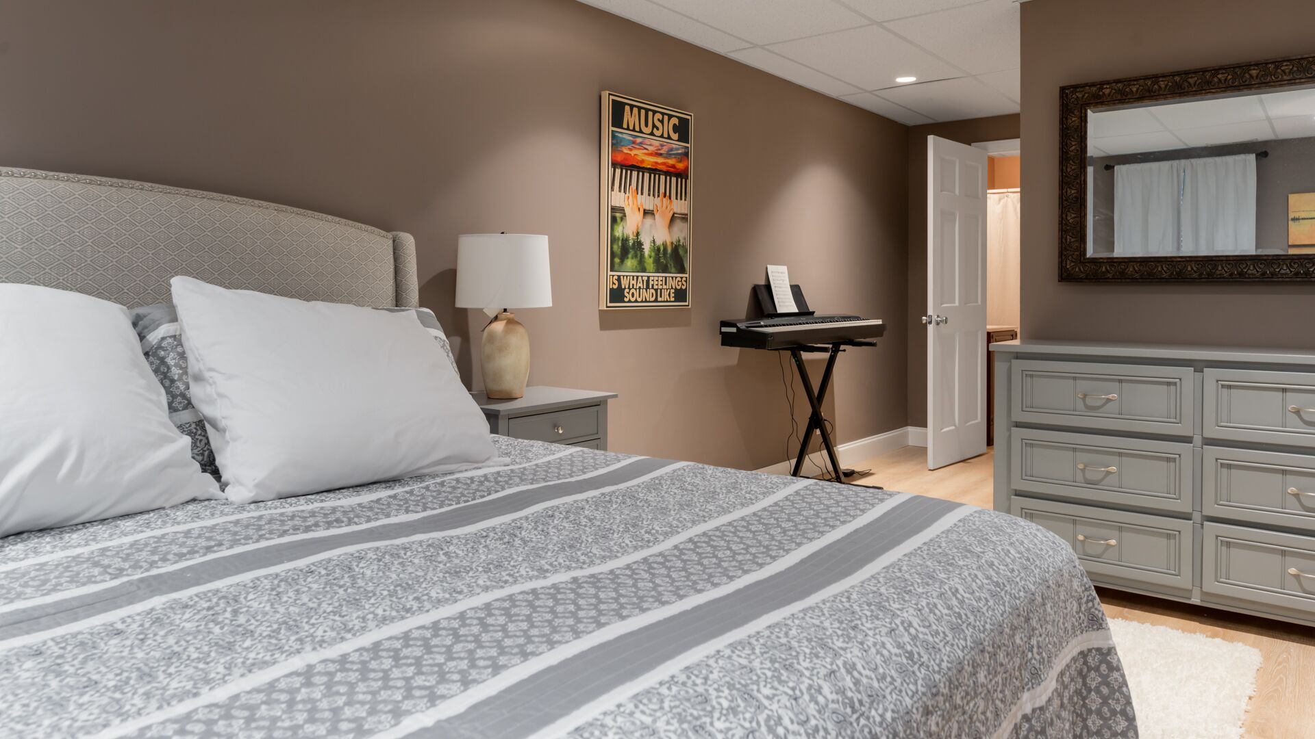 Une chambre à coucher avec un lit, une table de chevet, un bureau avec un clavier, une commode et une affiche accrochée au mur.