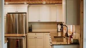 Cocina con techo de madera, armarios blancos, refrigerador de acero inoxidable, encimera de granito y alfombras estampadas.