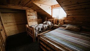 Un dormitorio de cabaña acogedor con cama alta, una cama más pequeña y una mesita de noche con lámpara.