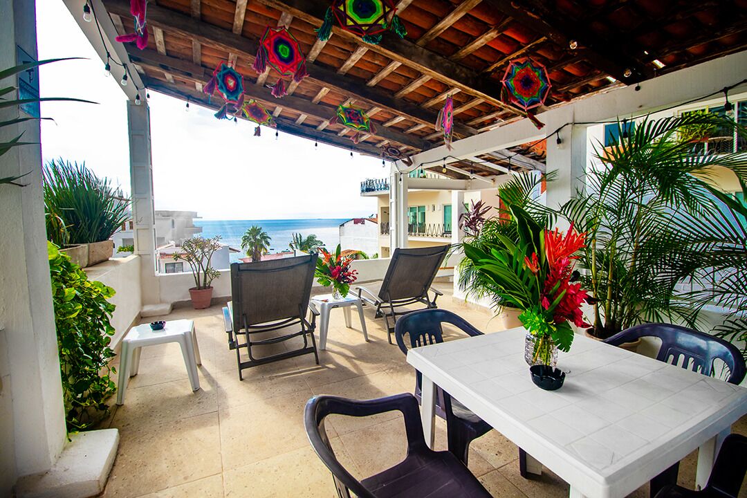 An outdoor patio with a table and chairs, potted plants, and a view of the ocean.