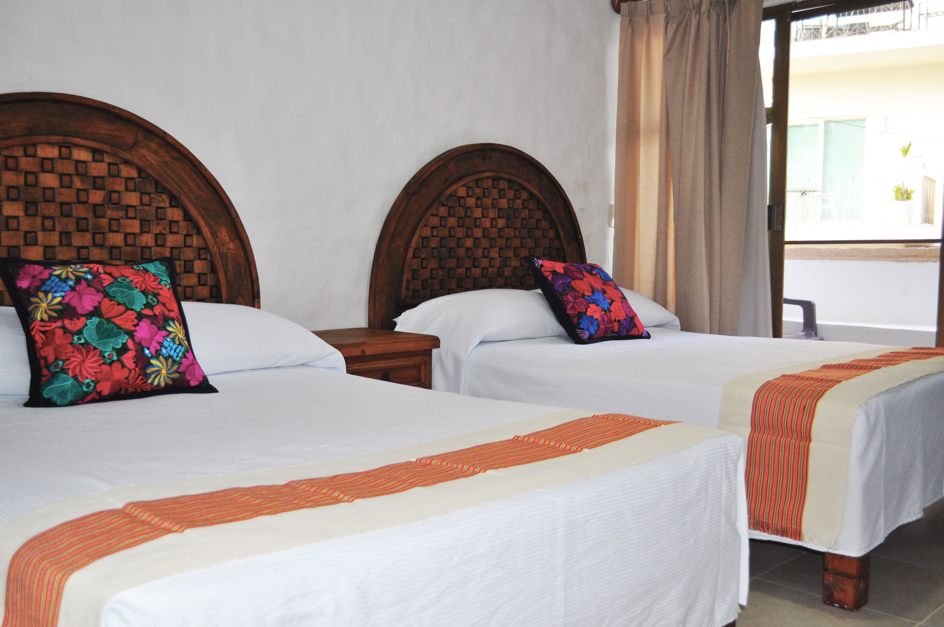 Dos camas con cabeceros de madera, ropa de cama blanca y almohadas florales coloridas.