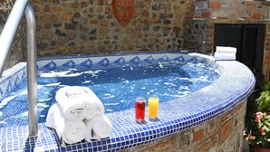 Ein Whirlpool mit Steinwänden, blauen Mosaikfliesen, einer Metallhandstange sowie Handtüchern und Getränken am Rand.