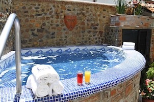 A stone-walled hot tub with blue mosaic tiles, a metal handrail, and towels and drinks on the edge.