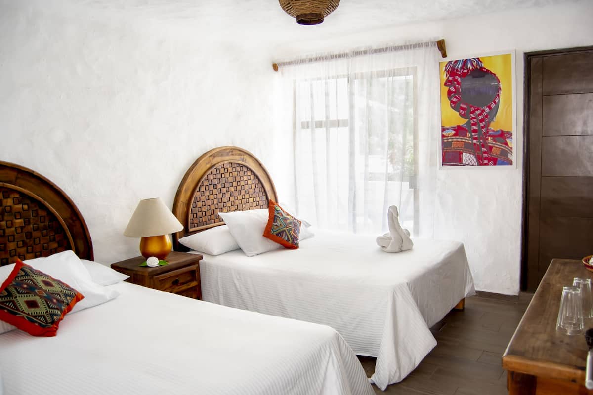 Une chambre d’hôtel avec deux lits, une tête de lit en bois, une table de chevet avec une lampe et un tableau au mur.