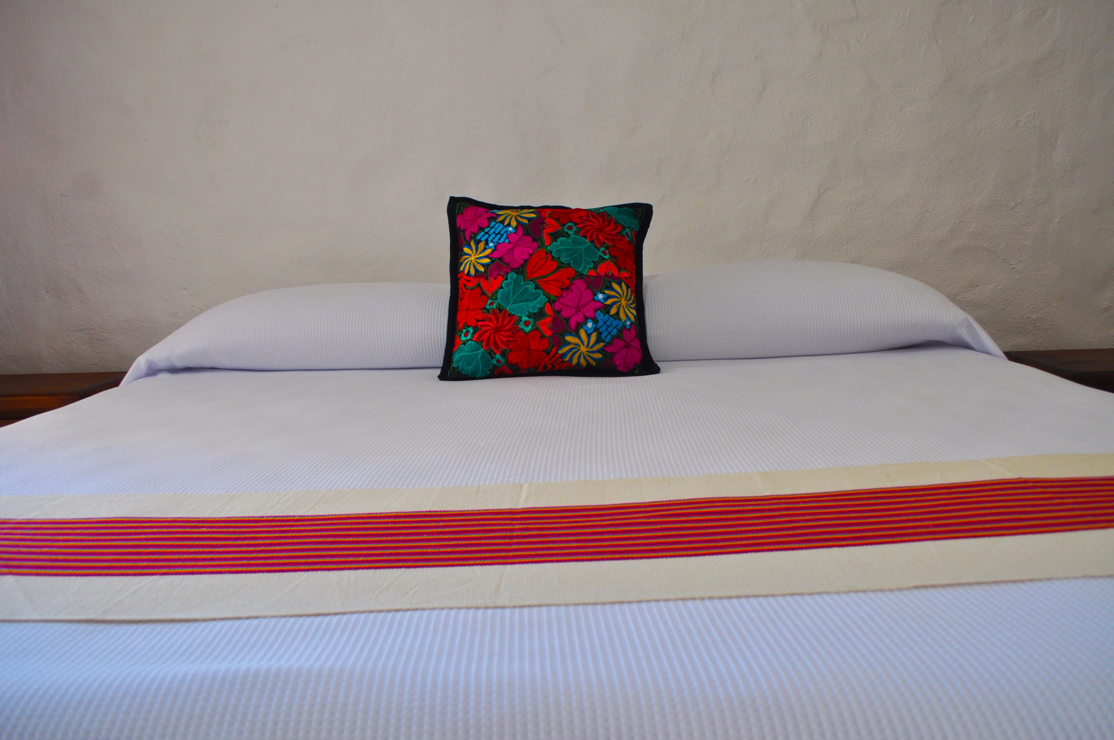 Una cama con un colchón blanco, una colcha a rayas rojas y blancas y una almohada colorida.