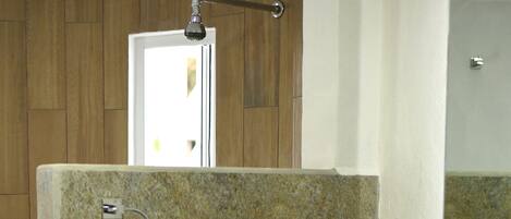 A bathroom with a stone wall, a white sink, and a towel dispenser.