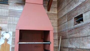 Un horno de pizza rojo al aire libre con chimenea, una pared de madera y una pequeña ventana.