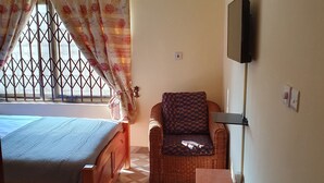 A compact room with a bed, a small table, and a window with a metal grid. - 2 bedroom apartment (North Legon)