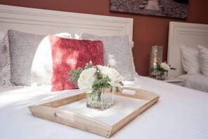 A neatly made bed with a wooden tray holding a vase of white flowers, set against a backdrop of patterned pillows and a red throw blanket. - Fort Lauderdale Beach, LAS OLAS, Big Heated Pool & 7 person hot tub (Fort Lauderdale)