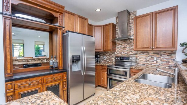 Cocina con encimeras de granito, electrodomésticos de acero inoxidable, armarios de madera y salpicadero con mosaicos.