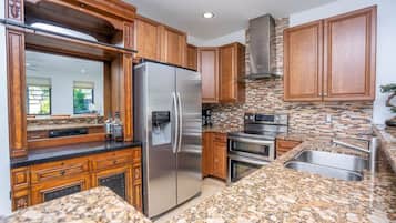 A kitchen with granite countertops, stainless steel appliances, wooden cabinets, and a backsplash with mosaic tiles.
