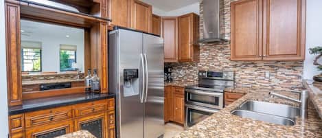 Cocina con encimeras de granito, electrodomésticos de acero inoxidable, armarios de madera y salpicadero con mosaicos.