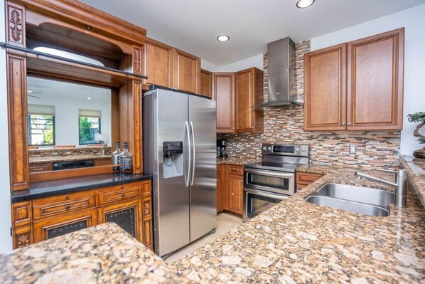 A kitchen with granite countertops, stainless steel appliances, wooden cabinets, and a backsplash with mosaic tiles. - Fort Lauderdale Beach, LAS OLAS, Big Heated Pool & 7 person hot tub (Fort Lauderdale)