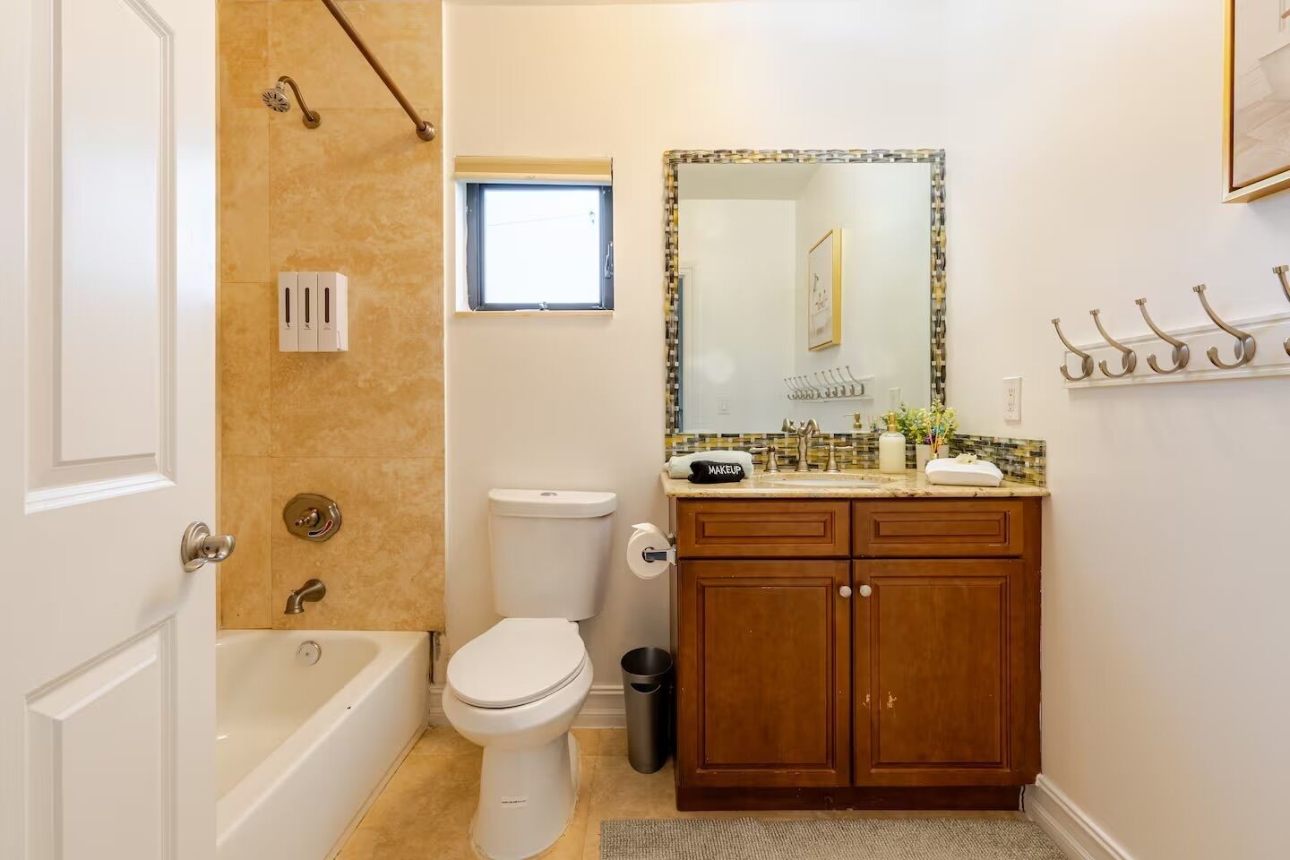 A bathroom with a bathtub, toilet, vanity with a mirror, and a window.