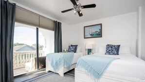 Una habitación de hotel con dos camas, un ventilador de techo, un amplio ventanal con cortinas y un cuadro en la pared.