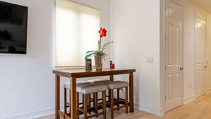 Una habitación con una mesa de comedor de madera, dos bancos acolchados, una planta en maceta y un televisor montado en la pared.