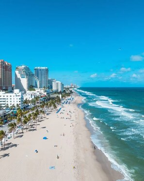 A beach with a cityscape in the background, including high-rise buildings and palm trees.