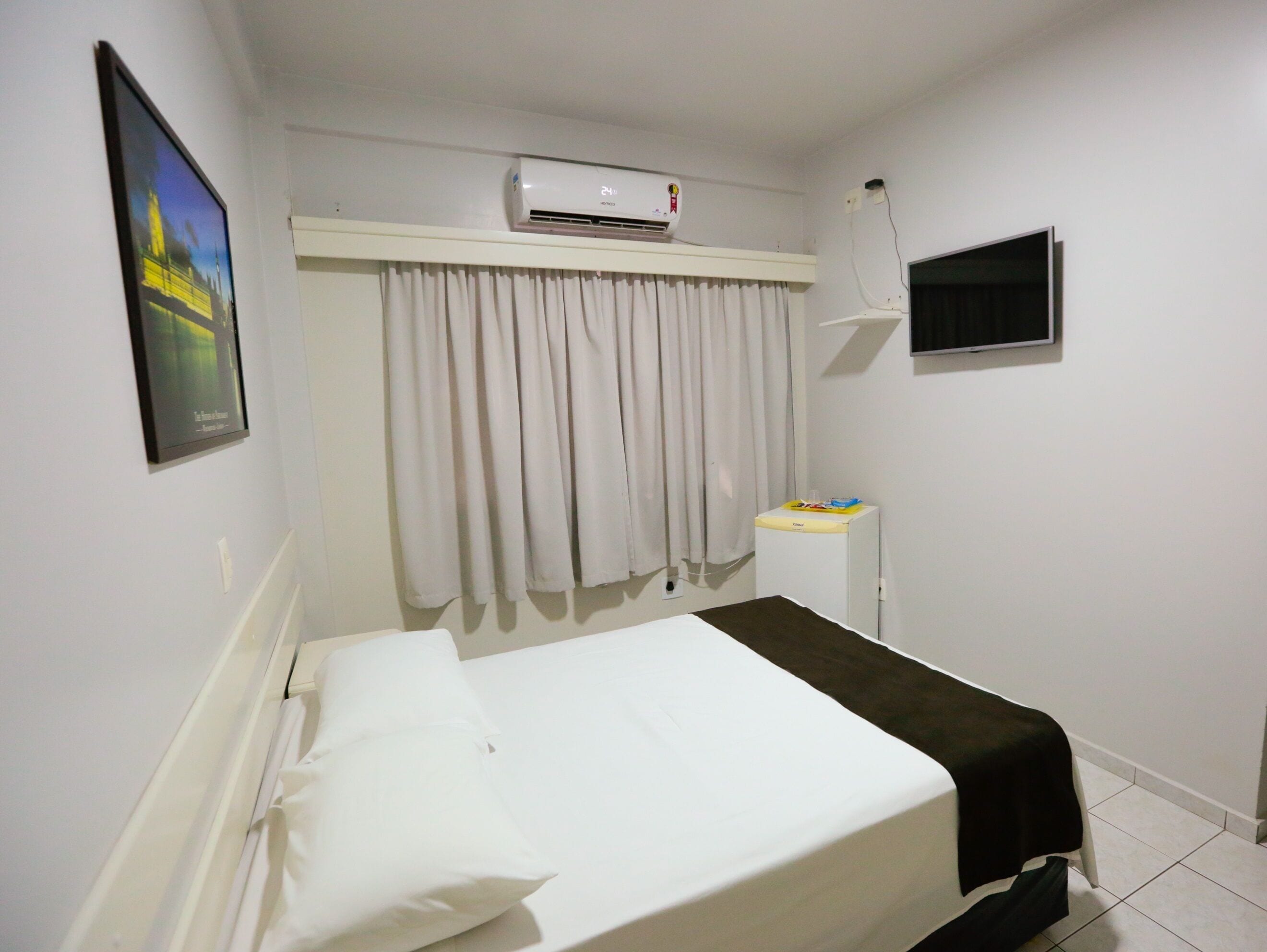 A hotel room with a bed, an air conditioner, a TV, and a small table with a tray.