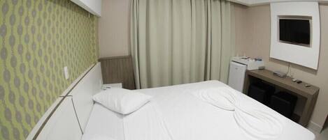A hotel room with a bed, a desk with a computer, a TV, and an air conditioner.