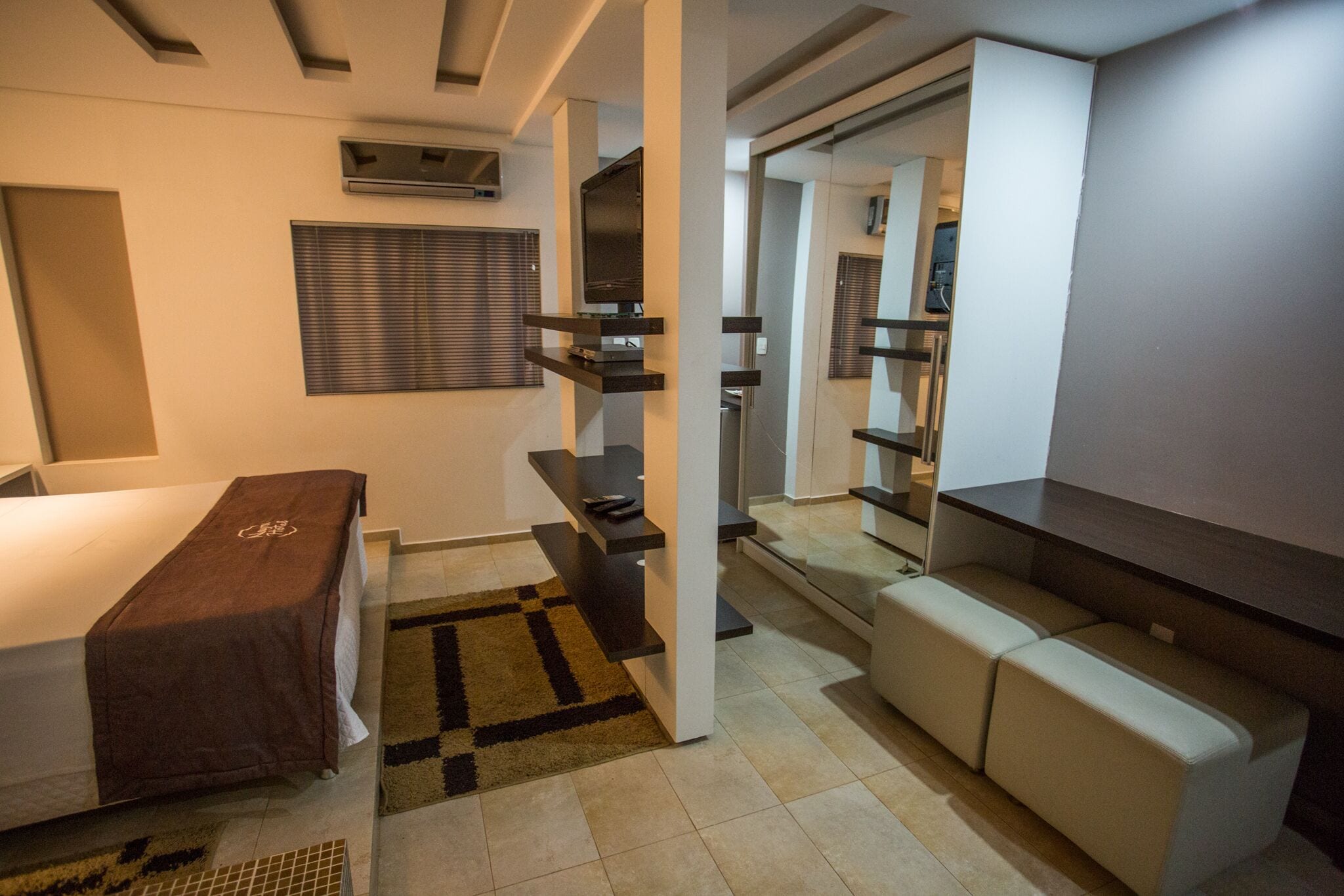 A modern hotel room with a bed, a sofa, a TV, and a mirror.