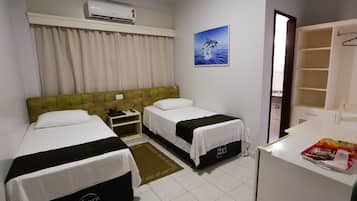 Habitación de hotel con dos camas, una mesita de noche, equipo de aire acondicionado, un cuadro con un delfín, baño con espejo y un pequeño escritorio con aperitivos.