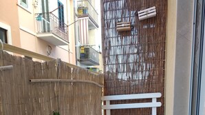 A narrow outdoor corridor with a wooden bench, a blue potted plant, and a bamboo fence. - ControVento Rooms (Margherita di Savoia)