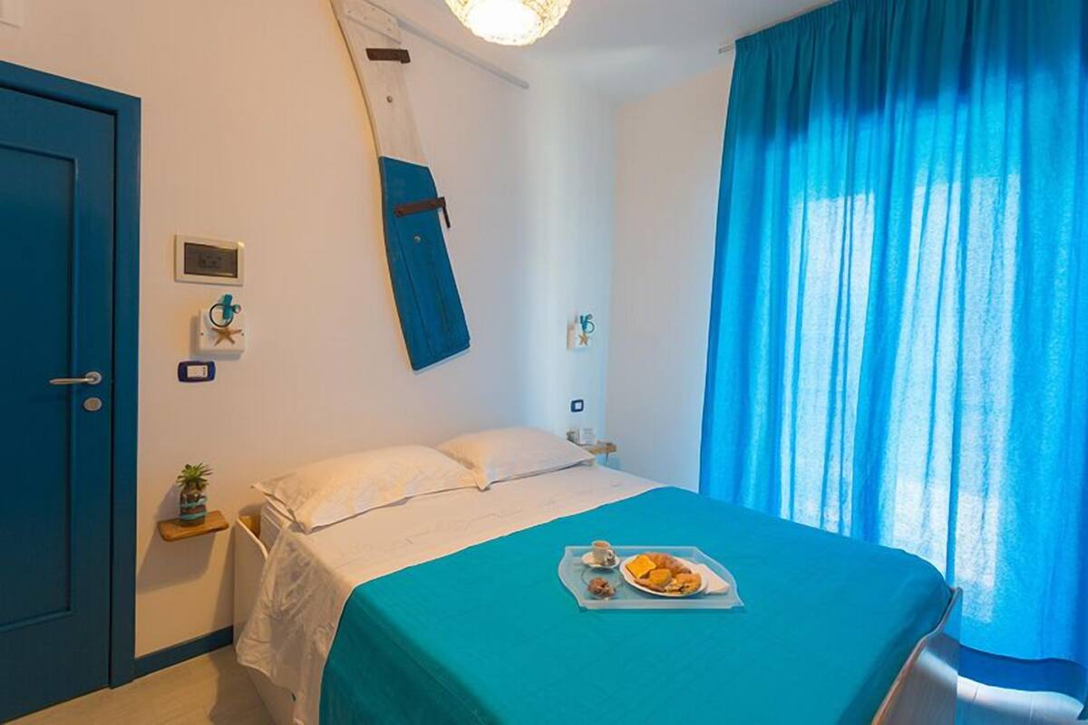 Une chambre d’hôtel avec un lit, une porte bleue, une petite plante et un plateau de petit-déjeuner posé sur le lit.