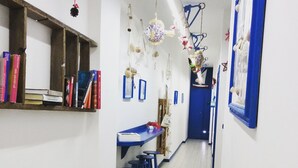 A narrow hallway with a blue counter and stools, a wooden shelf with books, and a blue door at the end. - ControVento Rooms (Margherita di Savoia)