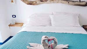 A bed with a teal quilt, a wooden headboard, and a towel arranged in a heart shape. - ControVento Rooms (Margherita di Savoia)