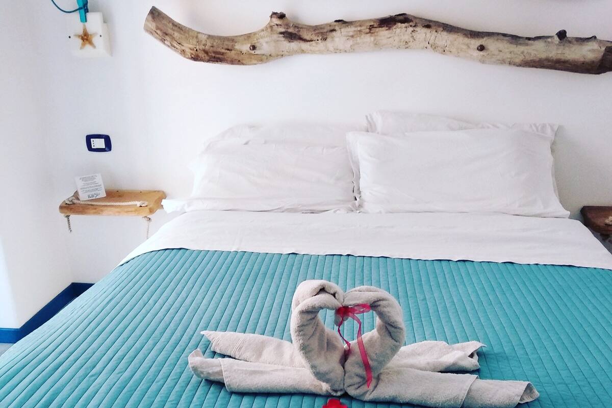 Un lit avec une couette turquoise, une tête de lit en bois et une serviette disposée en forme de cœur.