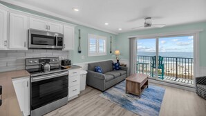 A modern kitchen with a microwave, stove, and oven, a gray sofa, and a view of the beach through a sliding glass door. - Direct OCEANFRONT Remodeled 4th Floor End Unit Myrtle Beach Resort (Myrtle Beach)