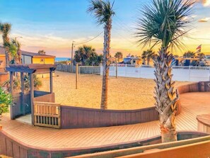 A beachside resort with a wooden deck, palm trees, and a fenced area.