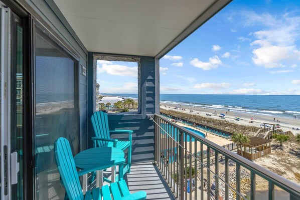 A balcony with turquoise chairs, a pool, and a beach view.