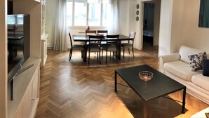 A modern living room with a herringbone floor, a black coffee table, a white sofa, and a dining area with a wooden table and chairs. - Apartment Rod Pena By Hart (Buenos Aires)