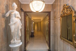 A marble hallway with statues, a chandelier, and ornate doors.