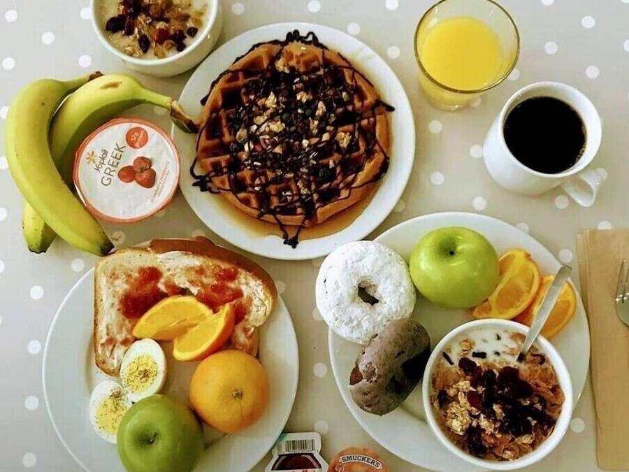 A breakfast table with various food items including a waffle, toast, yogurt, fruit, and a glass of orange juice.