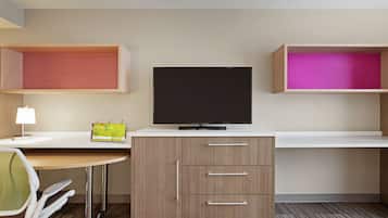 Una habitación de hotel con escritorio, televisión, silla y dos estantes con compartimentos.